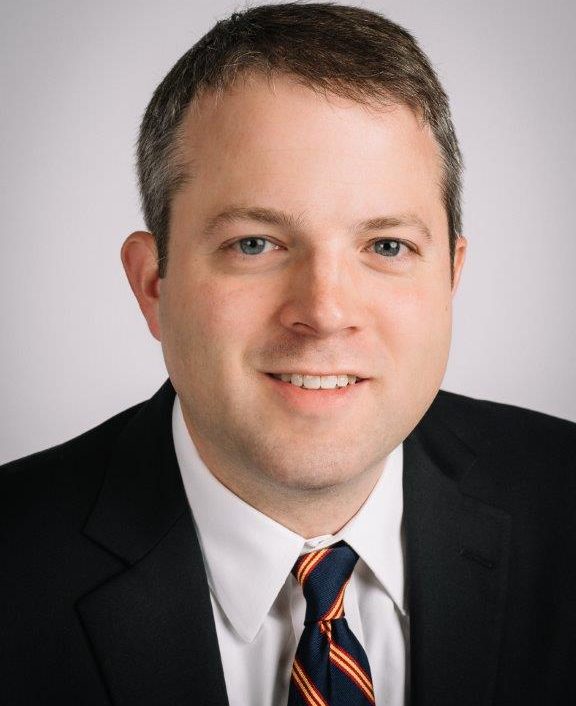 a man wearing a suit and tie smiling at the camera